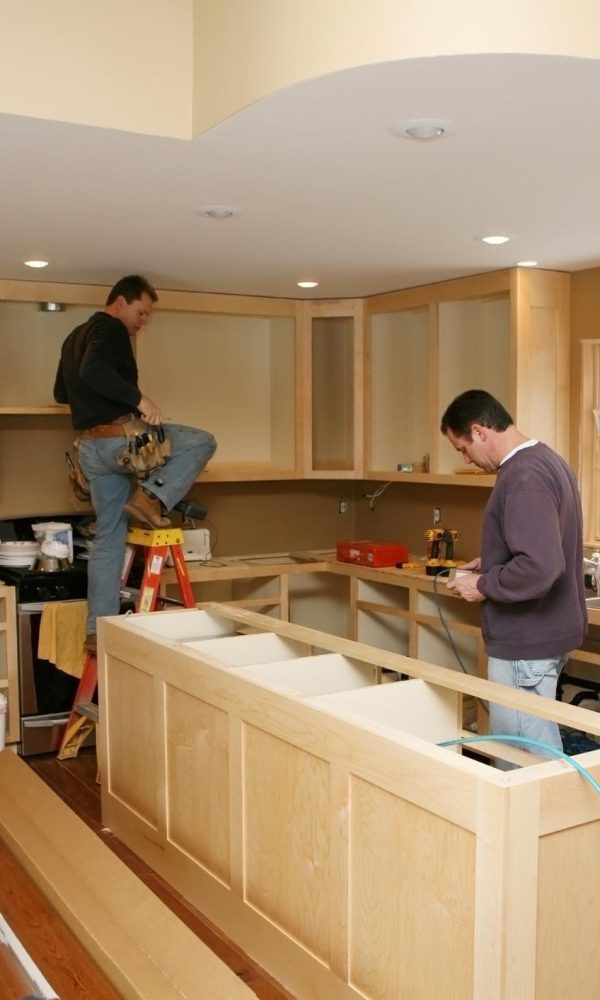 Cabinet maker installing custom made kitchen island and cabinets, while electrician installs in-cabinet lighting. 
Very shallow DOF quickly drops off to nice soft focus.